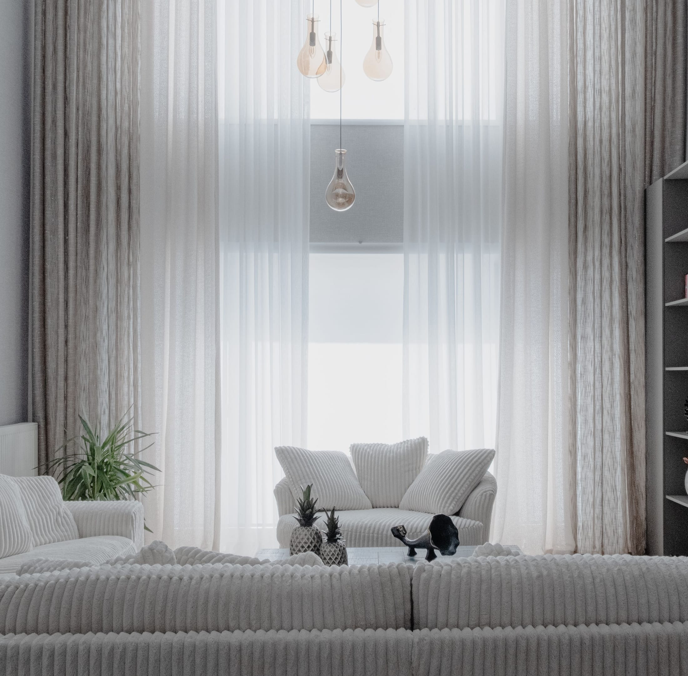 A bright modern living room with a white sofa and sheer curtains, staged for sale